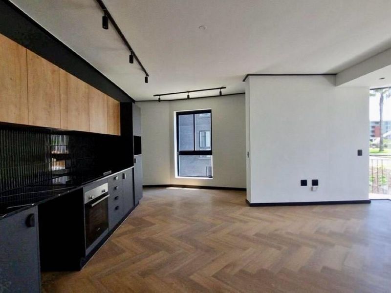 Modern open-plan living area featuring herringbone timber flooring, sleek built-in kitchen cabinetry, integrated oven, and large glass doors leading to an outdoor space.