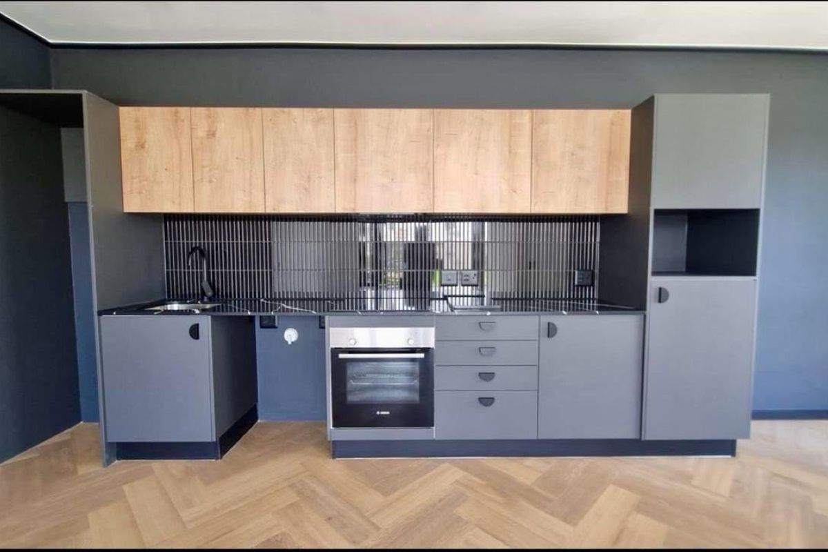 Modern kitchen featuring sleek grey cabinetry, wood-tone upper cabinets, a tiled backsplash, built-in oven, and stylish herringbone flooring.