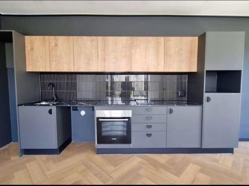 Modern kitchen featuring sleek grey cabinetry, wood-tone upper cabinets, a tiled backsplash, built-in oven, and stylish herringbone flooring.