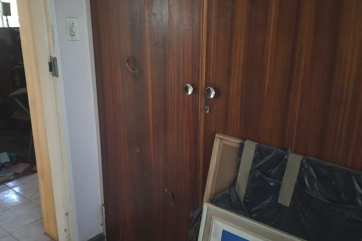 A bedroom interior featuring built-in wooden cupboards with visible wear and damage to the door finish.