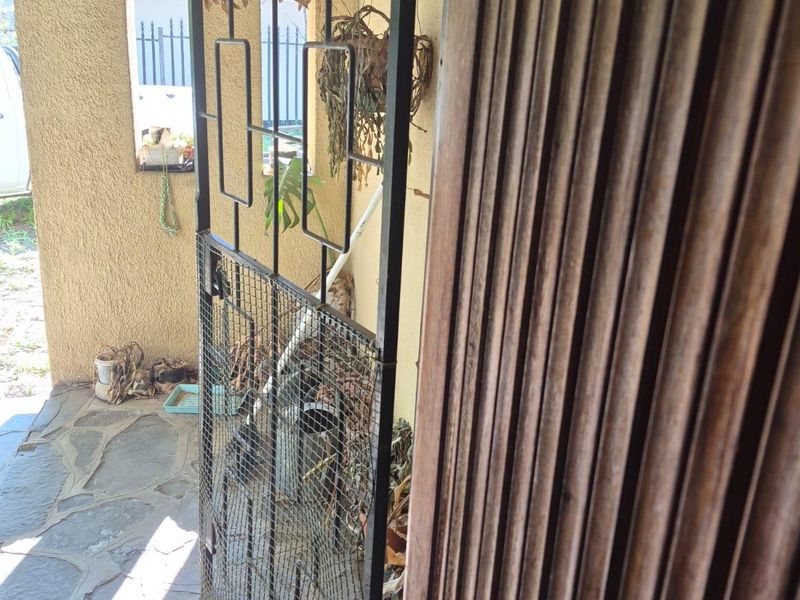 An exterior entrance area featuring a metal security gate and stone paved flooring, showing signs of weathering and wear.