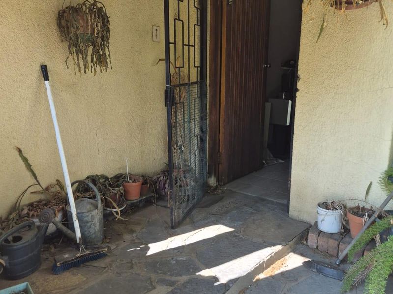 Entrance area featuring stone paving, a security gate, and a wooden door, requiring maintenance to the wall finish and flooring.
