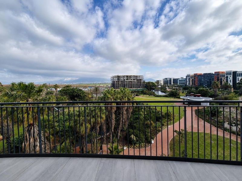 A scenic elevated view from a balcony overlooking a landscaped park, walking paths, and surrounding urban development.