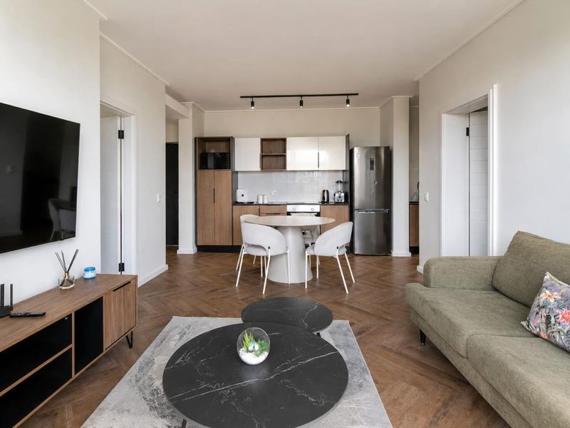 Modern open-plan living and kitchen area featuring elegant herringbone timber flooring, contemporary cabinetry, and integrated appliances in a well-maintained apartment setting.