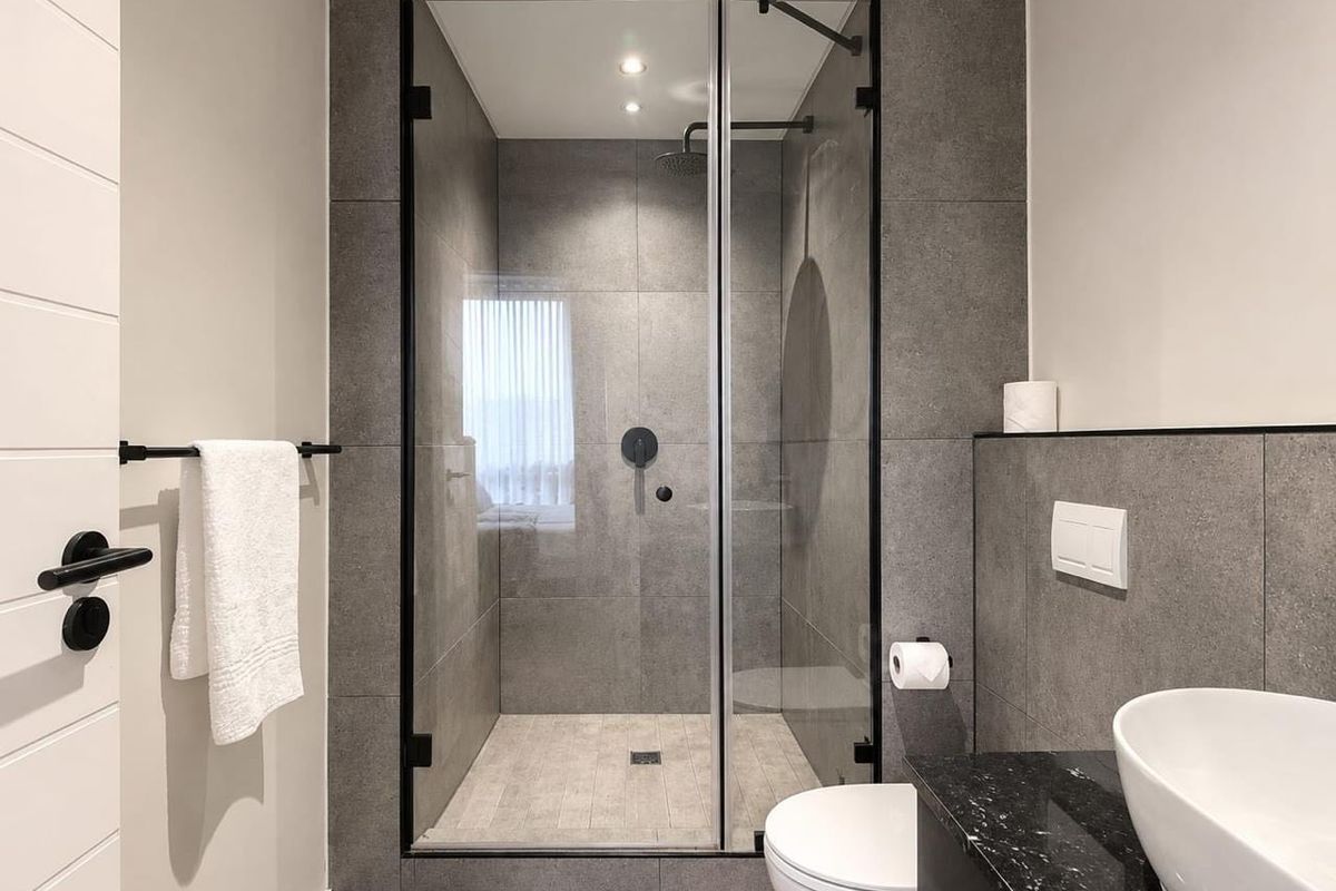 Modern bathroom featuring a walk-in shower with black fixtures, a wall-mounted toilet, and a sleek vessel sink on a stone vanity.