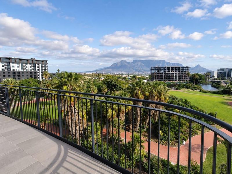 A scenic balcony view overlooking a landscaped park with palm trees and a clear view of Table Mountain in the distance.