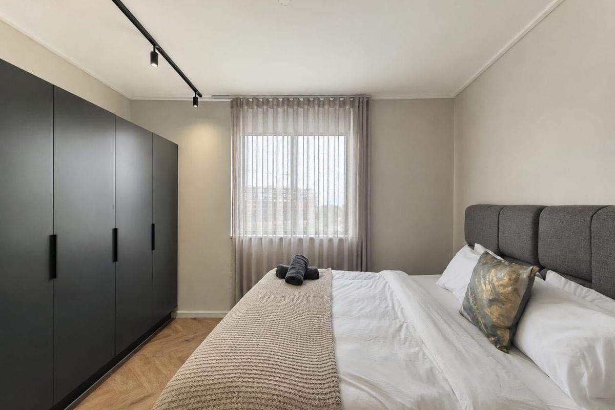 Modern bedroom featuring herringbone timber flooring, a large built-in wardrobe, and contemporary track lighting, creating a clean and well-maintained living space.