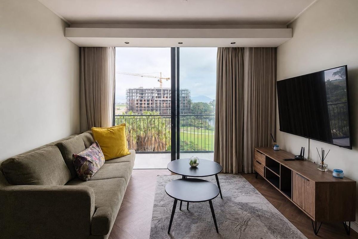 A modern living room featuring herringbone flooring, recessed ceiling lighting, and a large sliding glass door opening onto a balcony with scenic views.