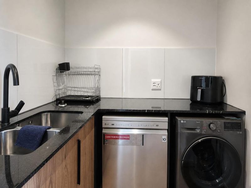 A modern, well-appointed laundry area featuring sleek cabinetry, granite countertops, a stainless steel sink, and integrated laundry appliances.