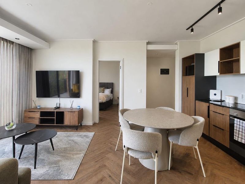 Modern open-plan living and dining area featuring herringbone timber flooring, contemporary kitchen cabinetry, and integrated appliances with a seamless flow to the bedroom.