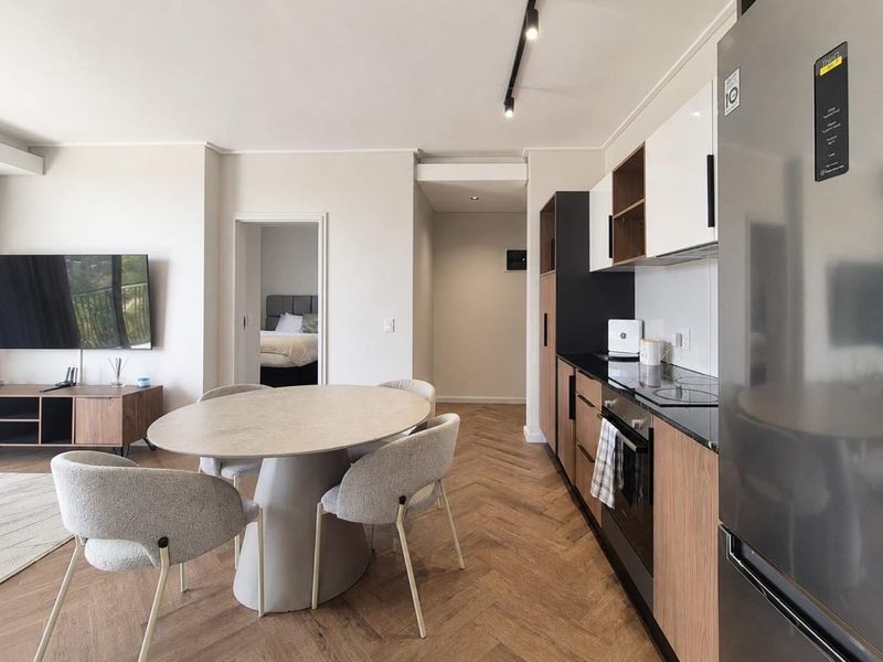 Modern open-plan living and kitchen area featuring herringbone timber flooring, sleek cabinetry, and integrated appliances, leading to a bedroom.