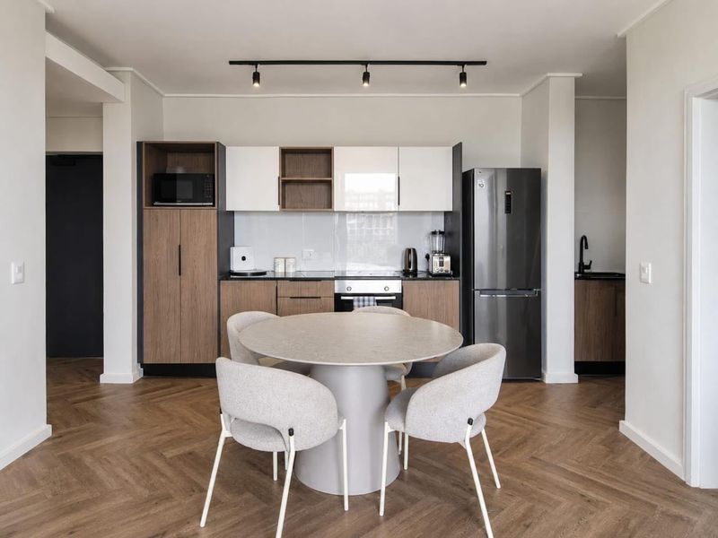 Modern open-plan kitchen and dining area featuring contemporary cabinetry, integrated appliances, track lighting, and stylish herringbone flooring.