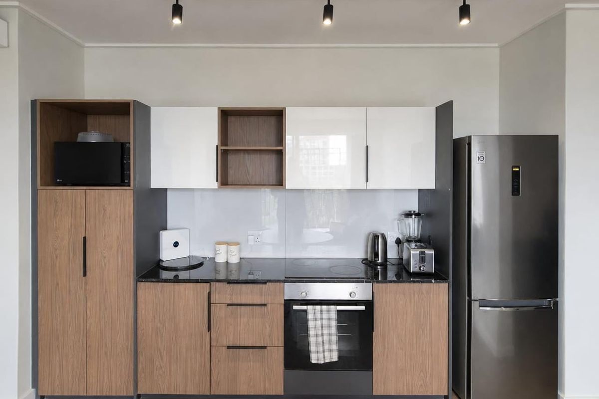 Modern kitchen featuring two-tone wood and white cabinetry, black stone countertops, integrated oven and hob, and contemporary track lighting.
