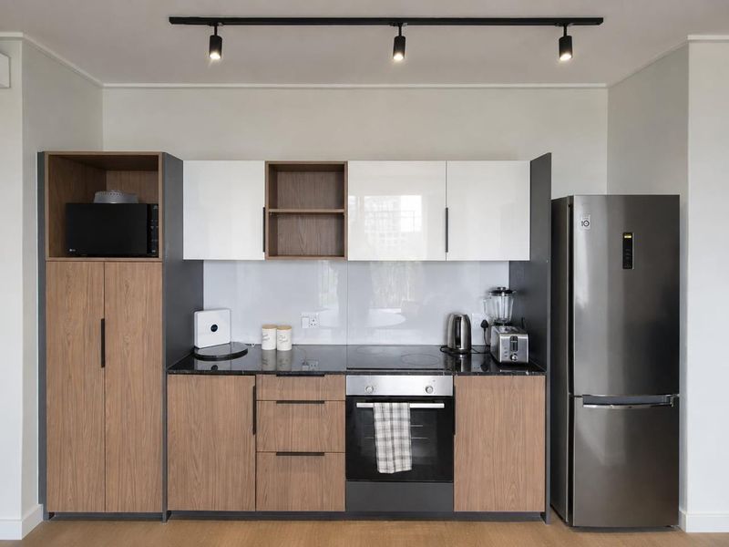 Modern kitchen featuring two-tone wood and white cabinetry, black stone countertops, integrated oven and hob, and contemporary track lighting.