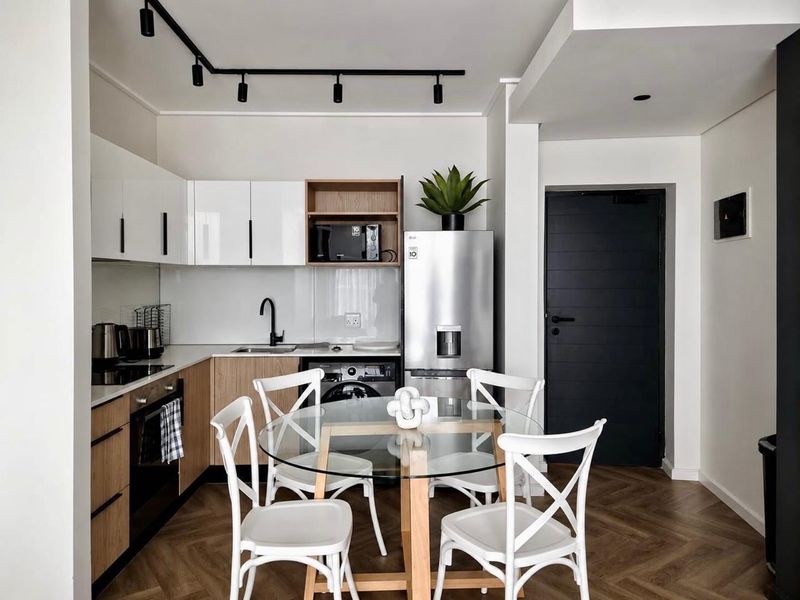 Modern open-plan kitchen featuring sleek cabinetry, integrated appliances, track lighting, and stylish herringbone flooring, seamlessly connected to the dining area.