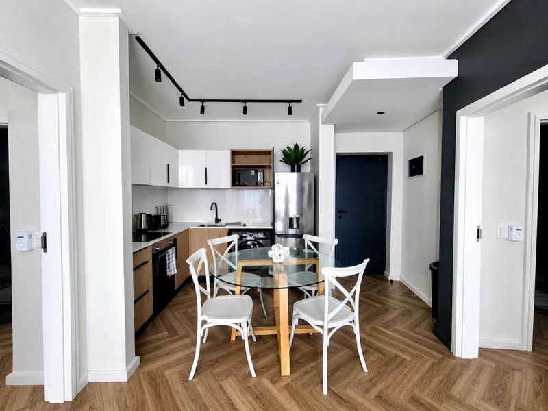 Modern open-plan kitchen featuring sleek cabinetry, track lighting, and herringbone laminate flooring, seamlessly integrated into the living space.