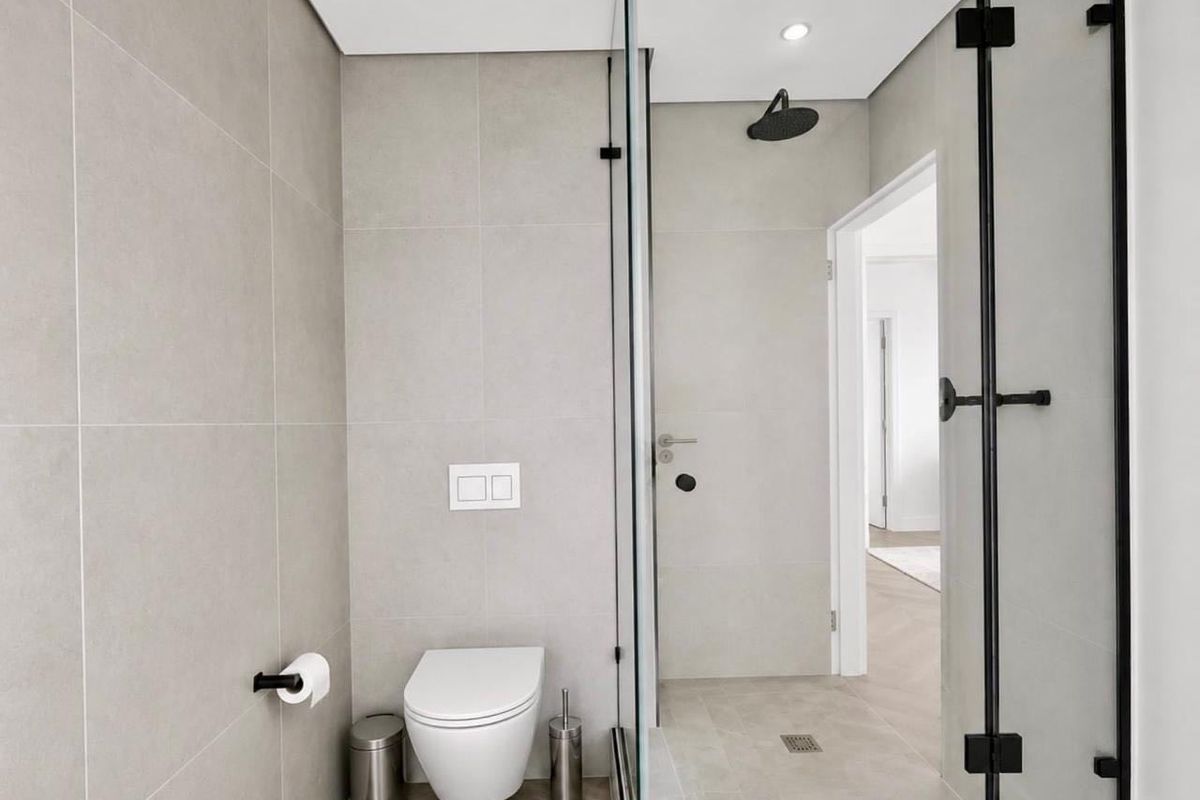Modern bathroom featuring a wall-mounted toilet, a glass-enclosed walk-in shower with a rain shower head, and neutral floor-to-ceiling tiling.