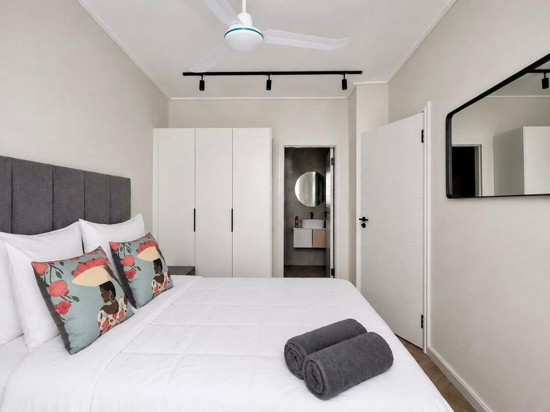 A modern, well-maintained bedroom featuring built-in wardrobes, a ceiling fan, track lighting, and direct access to an en-suite bathroom.
