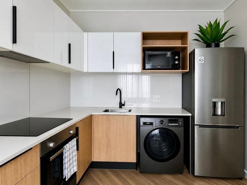 Modern kitchen featuring sleek white and wood-grain cabinetry, quartz countertops, integrated appliances, and high-quality finishes in a contemporary apartment setting.