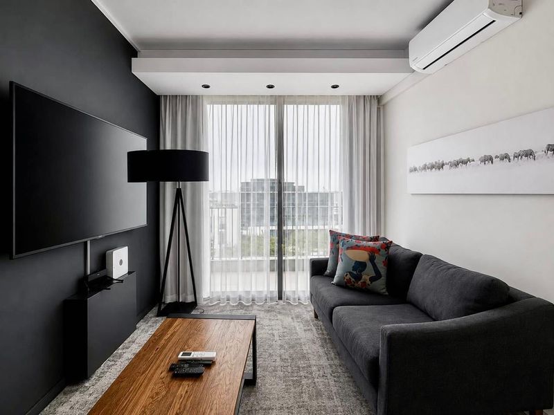 Modern living room featuring dark accent wall, recessed ceiling lighting, wall-mounted air conditioning, and sliding glass doors leading to a balcony.