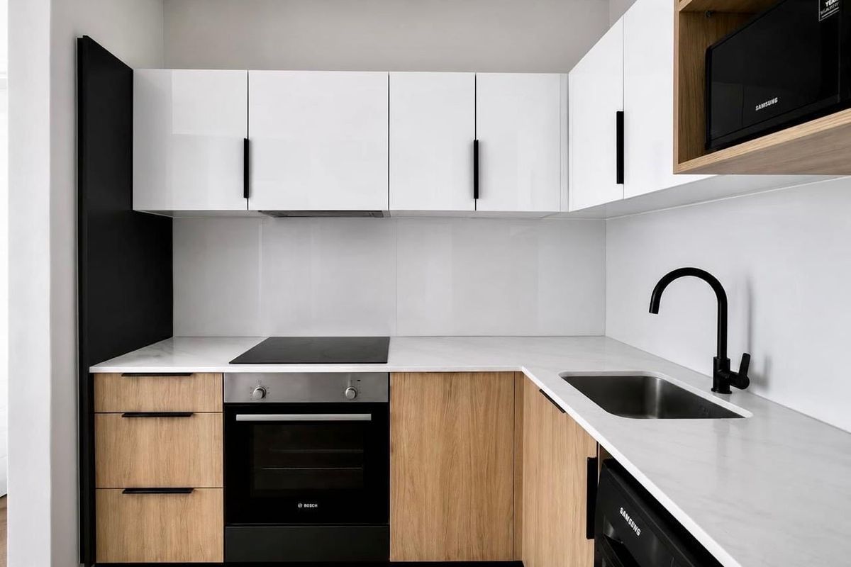 Modern kitchen featuring white and wood-tone cabinetry, stone countertops, integrated oven, electric hob, and a sleek black mixer tap.