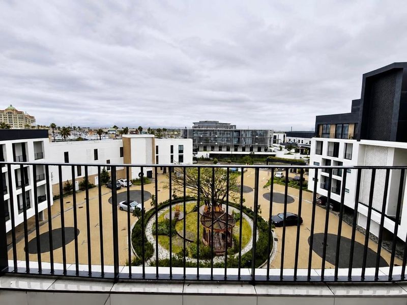 A modern balcony with a metal balustrade overlooking a landscaped courtyard and surrounding apartment complex.