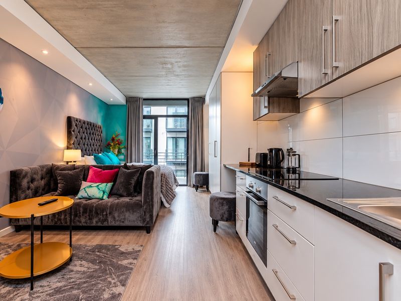 Modern open-plan studio apartment featuring an exposed concrete ceiling, sleek kitchen cabinetry with integrated appliances, and direct access to a private balcony.