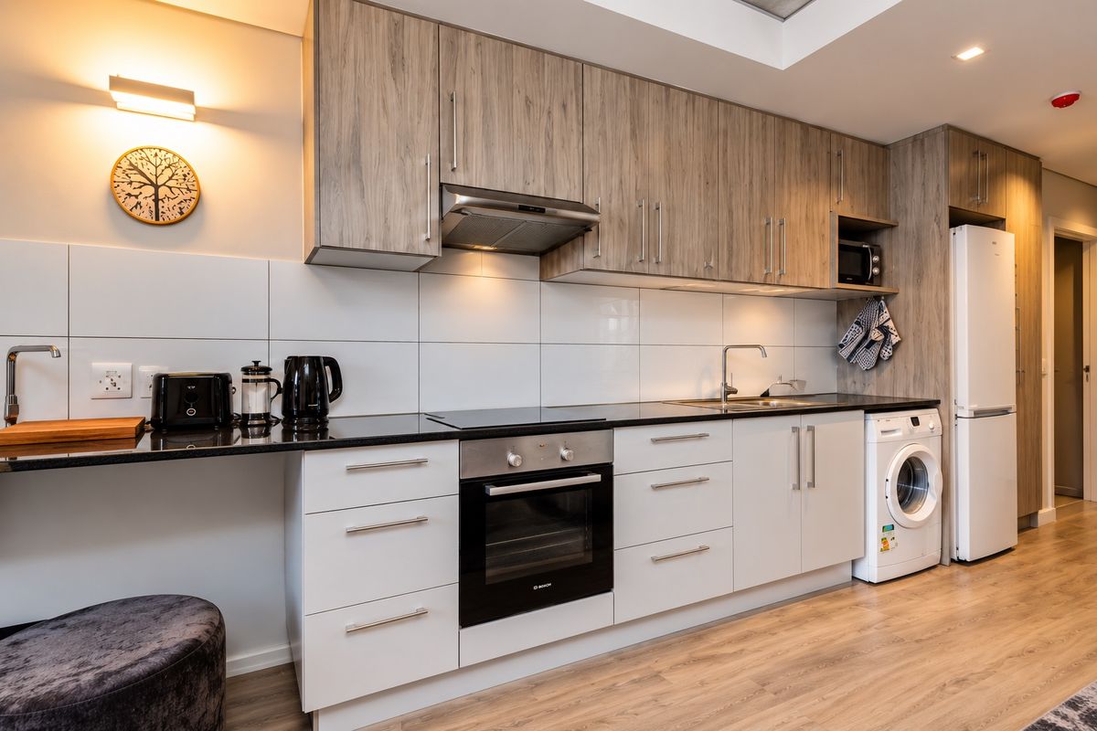 Modern kitchen featuring wood-grain upper cabinetry, white lower cabinets, black granite countertops, integrated oven, hob, extractor fan, and space for laundry appliances.