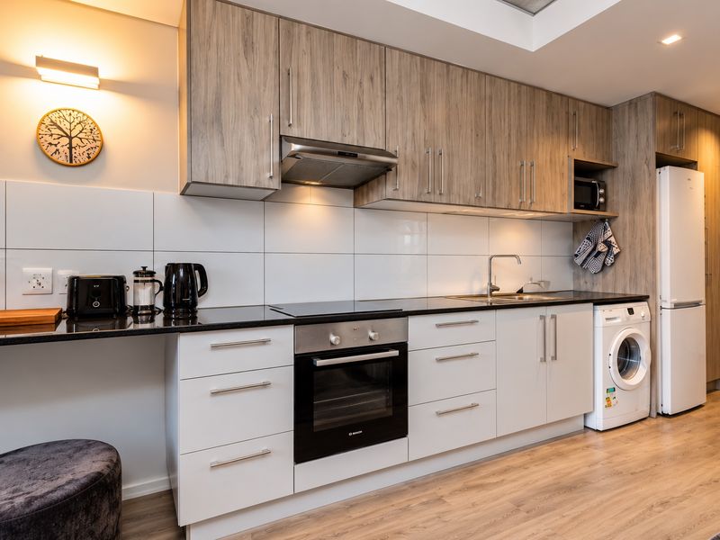 Modern kitchen featuring wood-grain upper cabinetry, white lower cabinets, black granite countertops, integrated oven, hob, extractor fan, and space for laundry appliances.