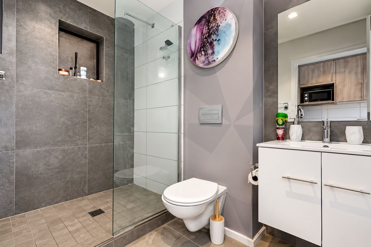 Modern bathroom featuring a walk-in shower with glass screen, wall-mounted toilet, and a sleek vanity unit with integrated storage and mirror.