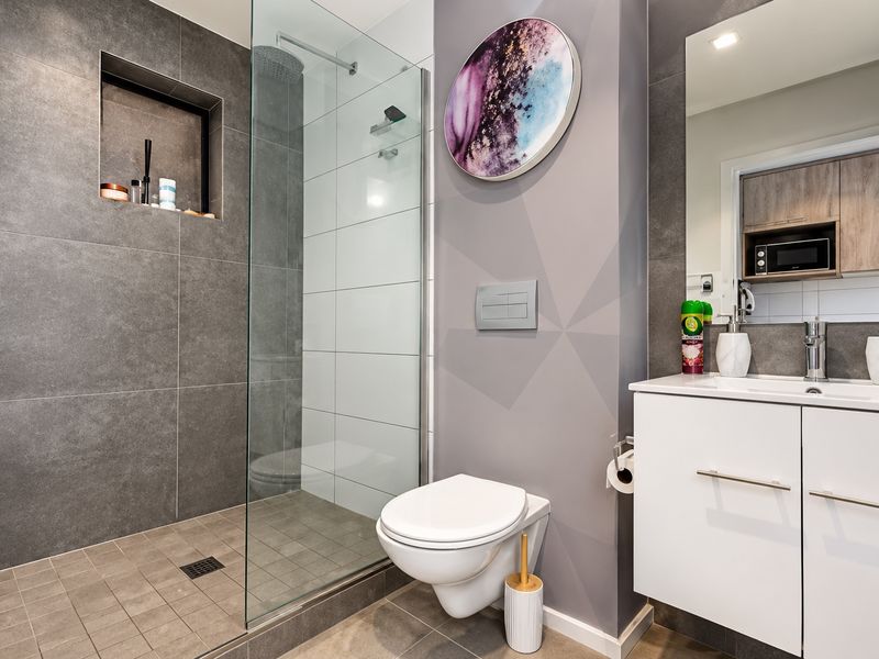 Modern bathroom featuring a walk-in shower with glass screen, wall-mounted toilet, and a sleek vanity unit with integrated storage and mirror.