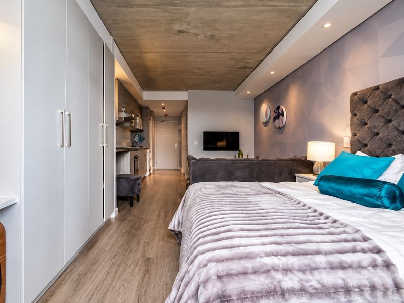 Modern open-plan studio apartment featuring an exposed concrete ceiling, sleek built-in cabinetry, and high-quality laminate flooring throughout the living and sleeping area.