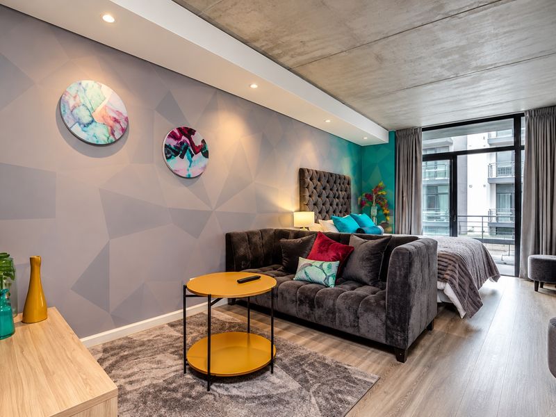 Modern open-plan studio apartment featuring an exposed concrete ceiling, contemporary geometric wallpaper, and direct access to a private balcony.