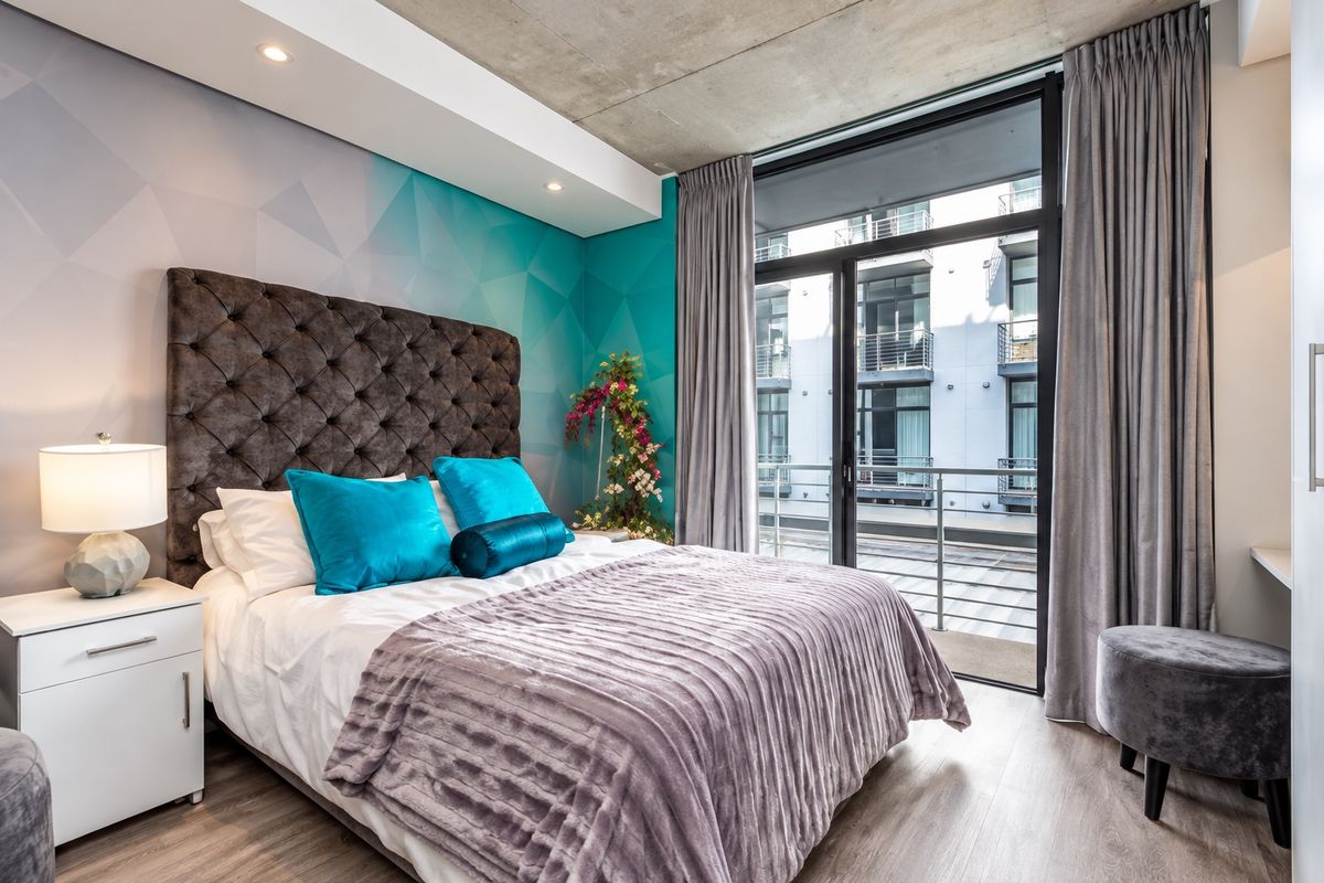Modern bedroom featuring an exposed concrete ceiling, recessed lighting, and a large sliding glass door providing access to a private balcony.