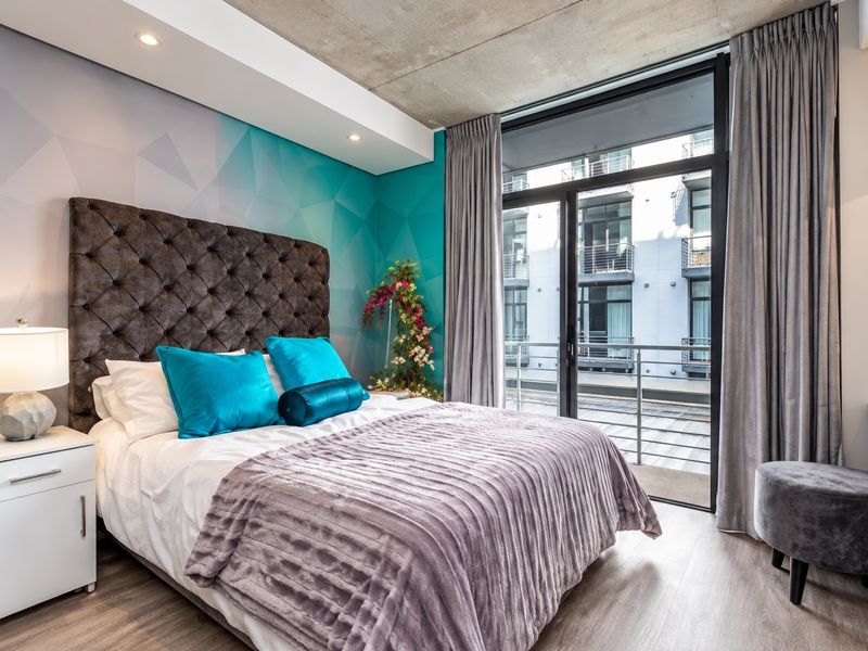 Modern bedroom featuring an exposed concrete ceiling, recessed lighting, and a large sliding glass door providing access to a private balcony.