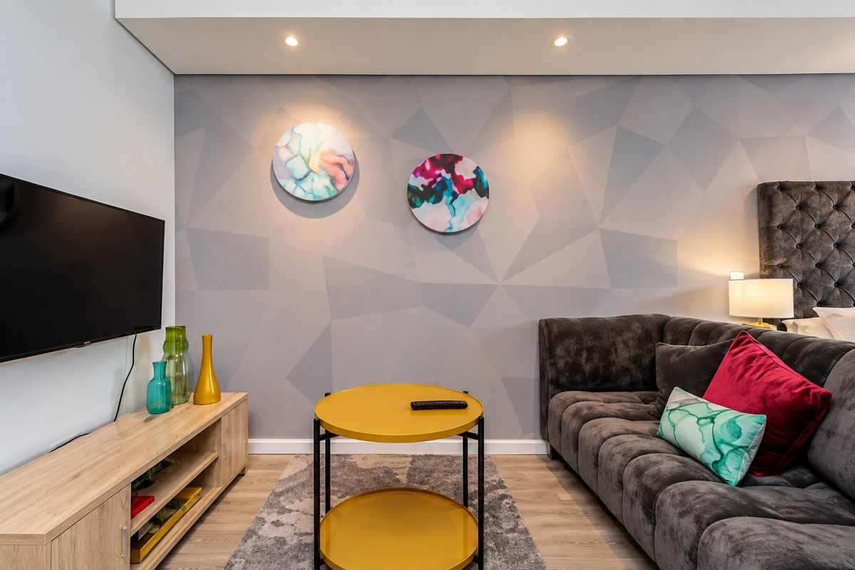 A modern living room featuring laminate flooring, recessed downlights, and a stylish geometric feature wall.