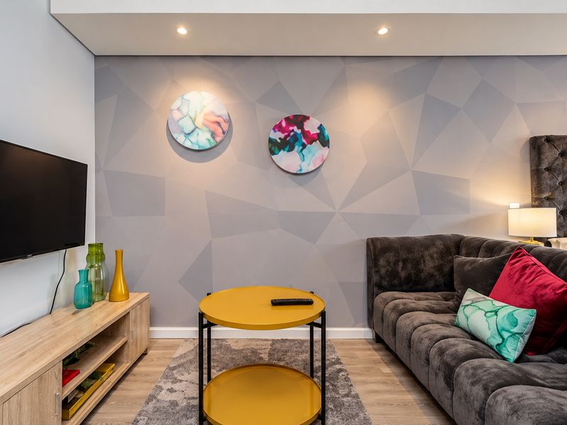 A modern living room featuring laminate flooring, recessed downlights, and a stylish geometric feature wall.