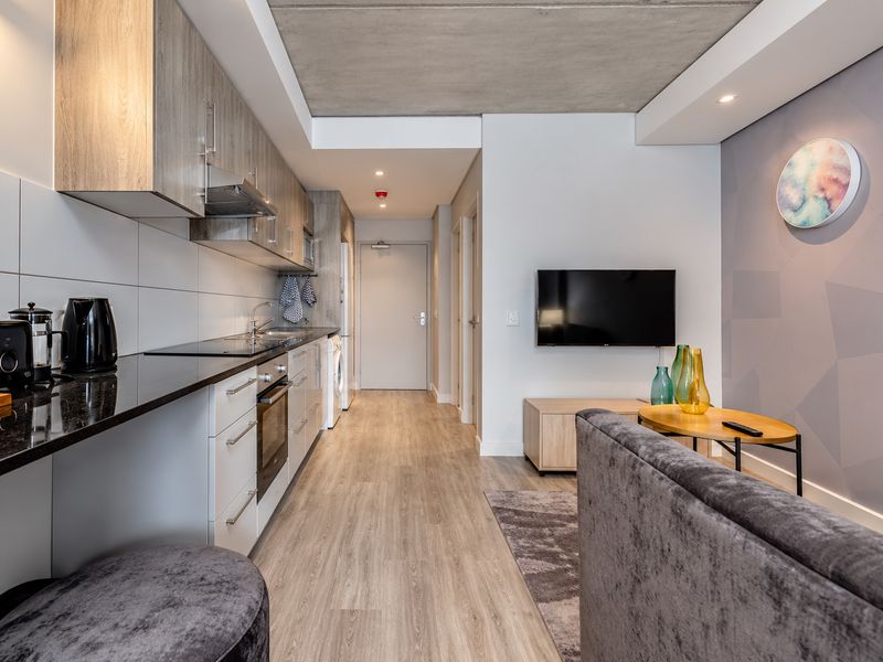 Modern open-plan apartment featuring a sleek kitchen with stone countertops, integrated appliances, and an exposed concrete ceiling, flowing into a comfortable living area.