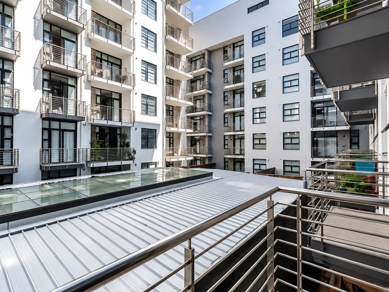 View of the apartment complex rear facade featuring multiple balconies, metal railings, and a large skylight over the lower roof section.