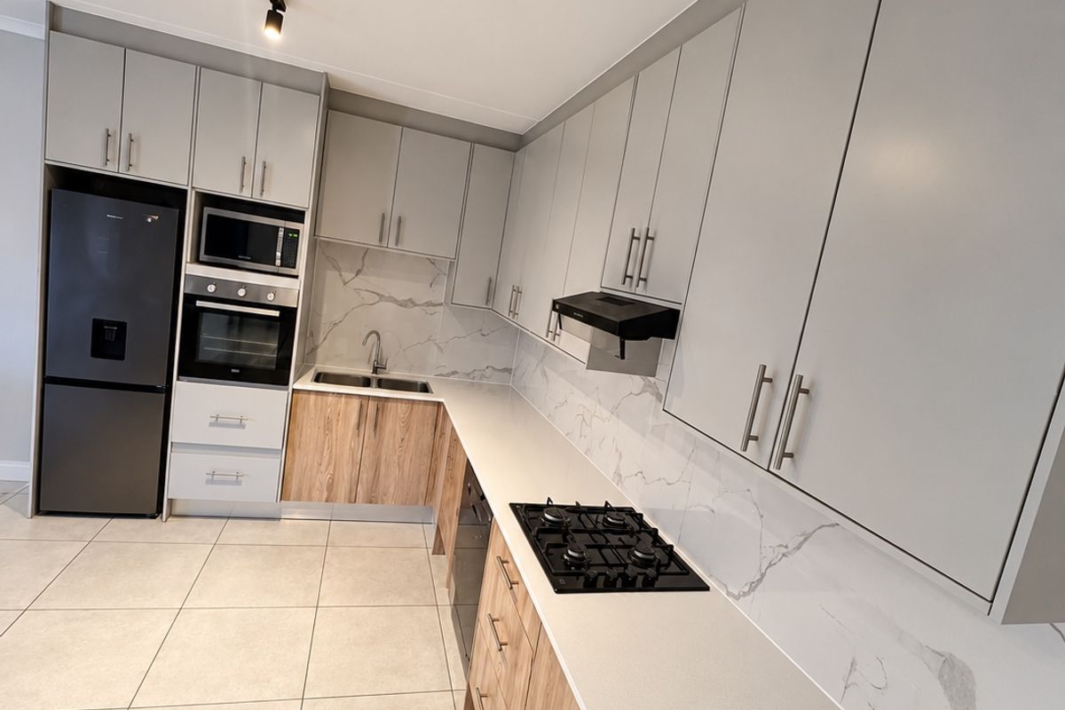 Modern kitchen featuring two-tone cabinetry, stone countertops with marble-look splashback, gas hob, built-in oven, and integrated microwave, complemented by neutral floor tiles.