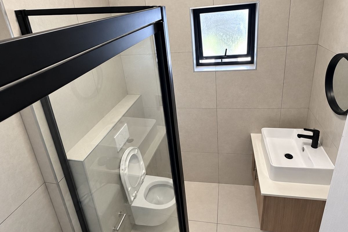 A modern, well-maintained bathroom featuring a walk-in shower with a black frame, a wall-mounted toilet, and a contemporary vanity with a vessel sink.