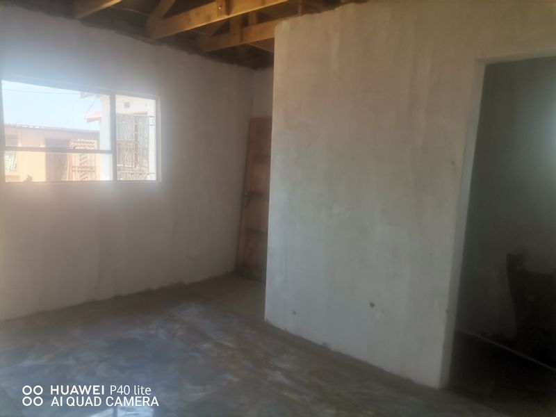 An unfinished bedroom interior featuring exposed timber roof trusses, bare plastered walls, and concrete flooring, offering a blank canvas for renovation.