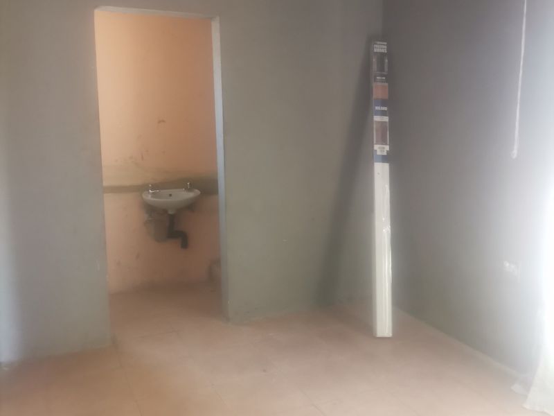 An empty bedroom featuring tiled flooring and an adjoining small wash area with a wall-mounted basin.
