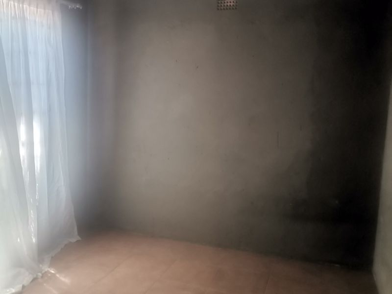 An empty bedroom featuring tiled flooring and an unfinished plastered wall, requiring final paint or decorative finishes.
