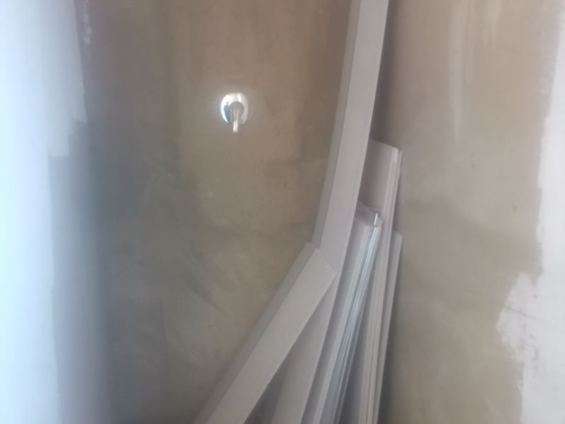 An unfinished bathroom space featuring a shower mixer and floor drain, currently undergoing renovation with exposed plaster walls.