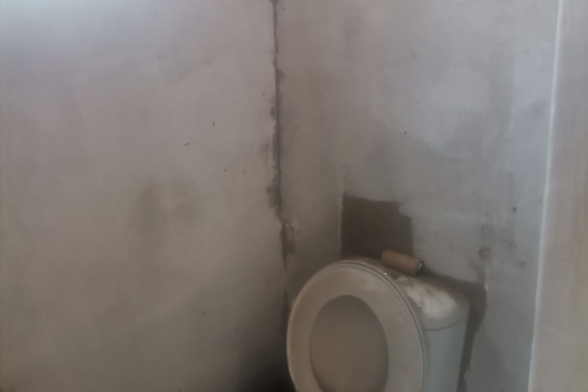 A small bathroom space featuring a toilet, currently in an unfinished state with exposed plaster walls requiring completion.