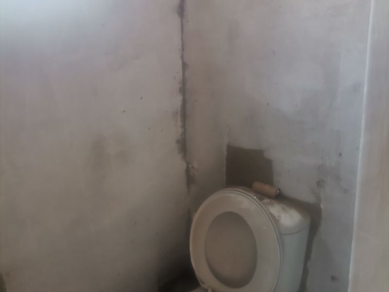 A small bathroom space featuring a toilet, currently in an unfinished state with exposed plaster walls requiring completion.