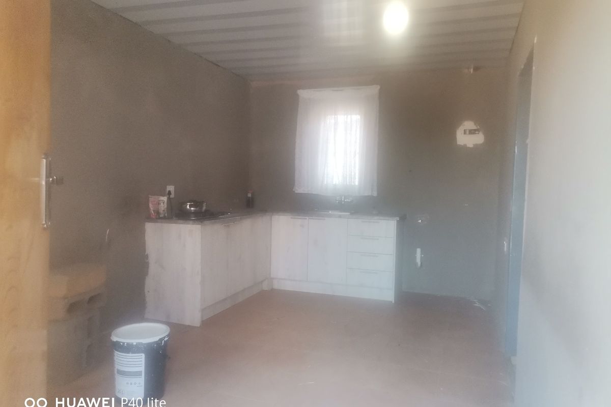 A basic, unfinished kitchen area featuring built-in cabinetry, a sink, and a cooktop, requiring cosmetic completion and wall finishing.