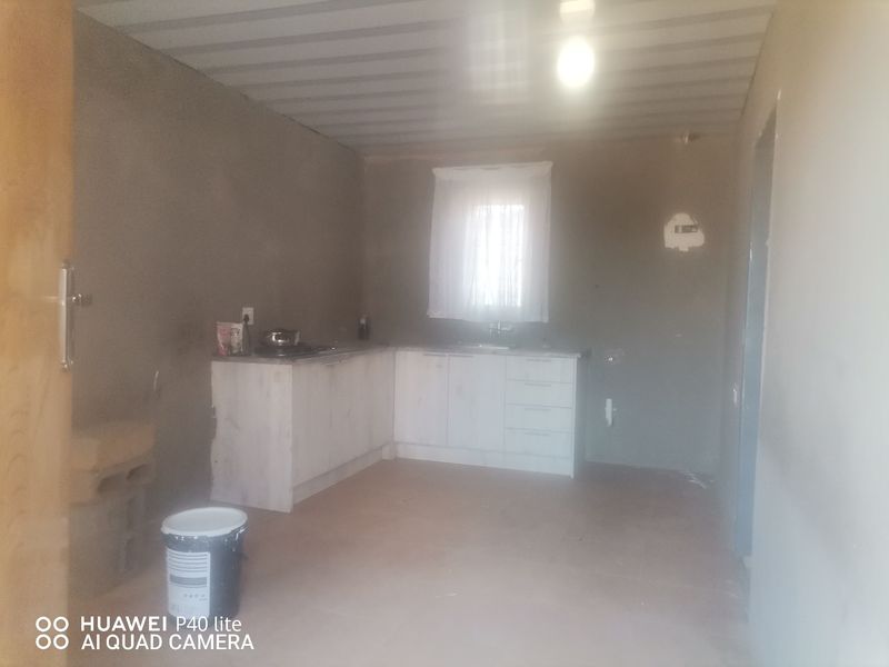 A basic, unfinished kitchen area featuring built-in cabinetry, a sink, and a cooktop, requiring cosmetic completion and wall finishing.
