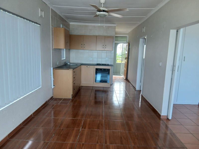 Open-plan kitchen and living area featuring tiled flooring, built-in cabinetry with integrated oven and hob, and a ceiling fan.